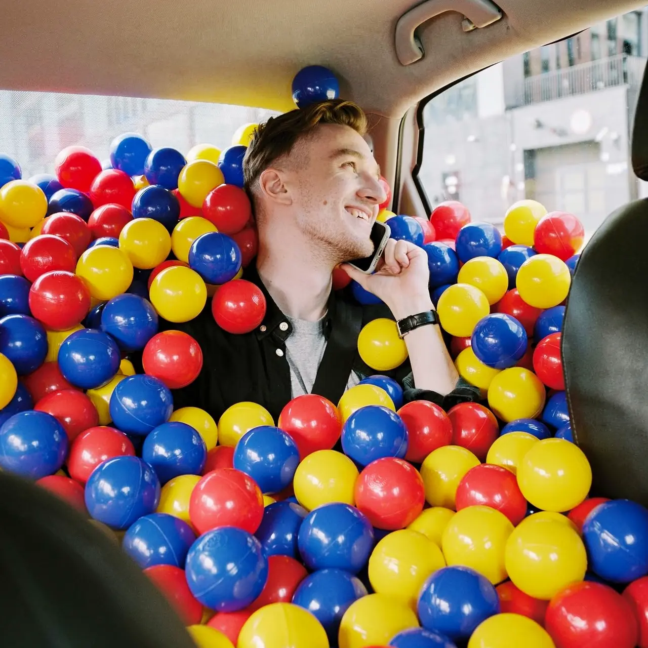 A photorealistic FLUX.2 example: a smiling man in a car filled with colorful ball-pit balls.